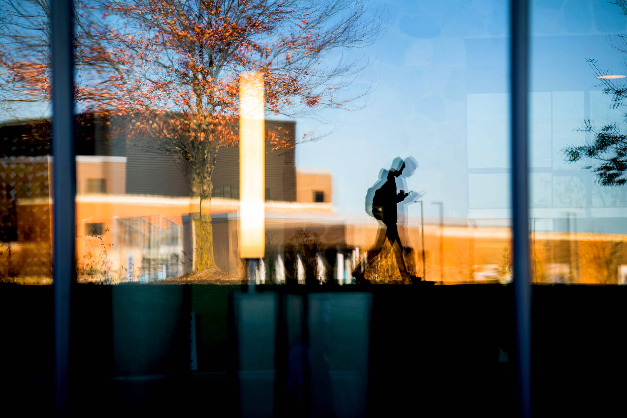 A student in shadow walks past the window with the Science Building in its reflection